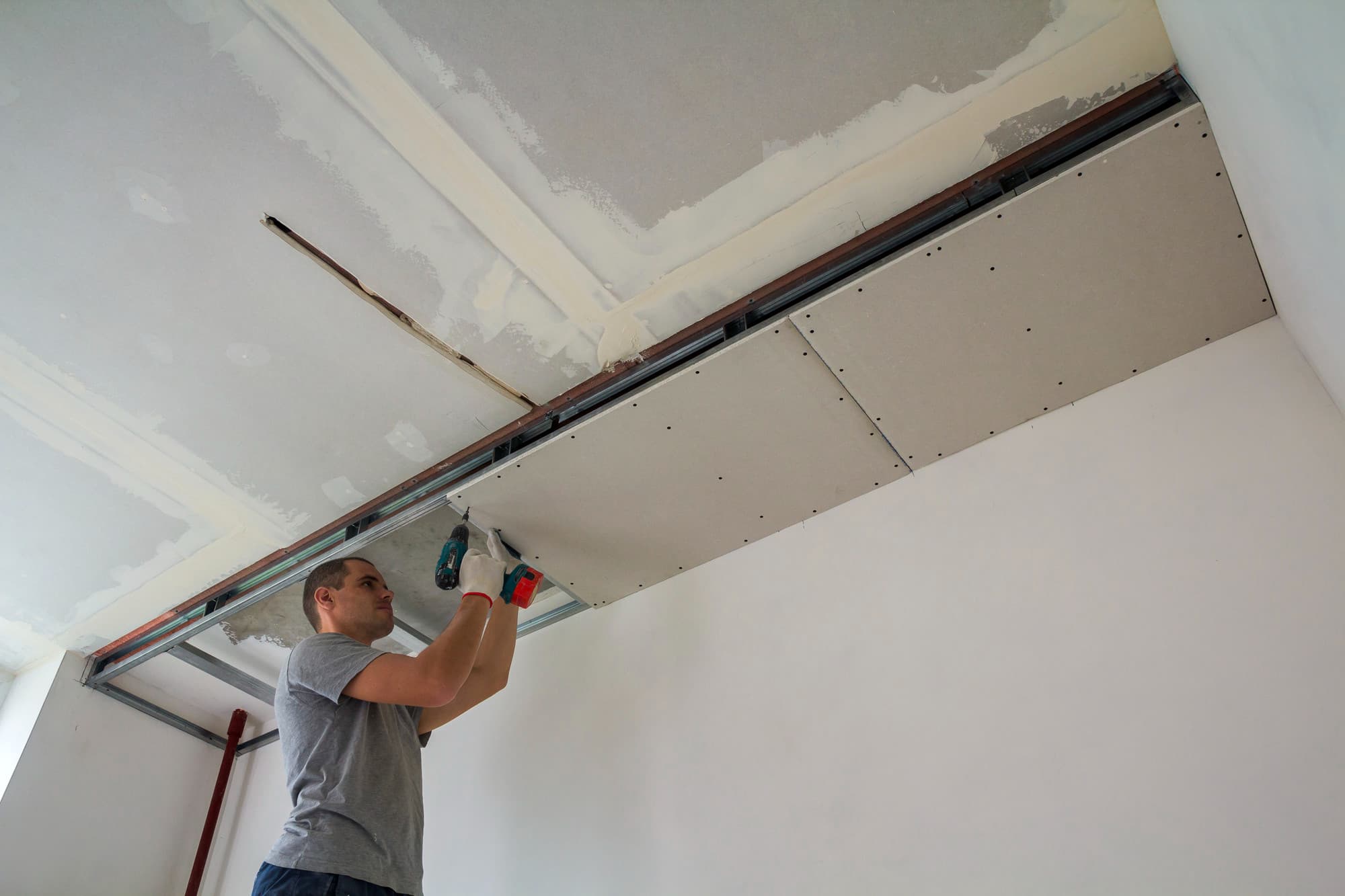 Handwerker verschraubt eine Gipskartonplatte an der Unterkonstruktion einer abgehängten Decke